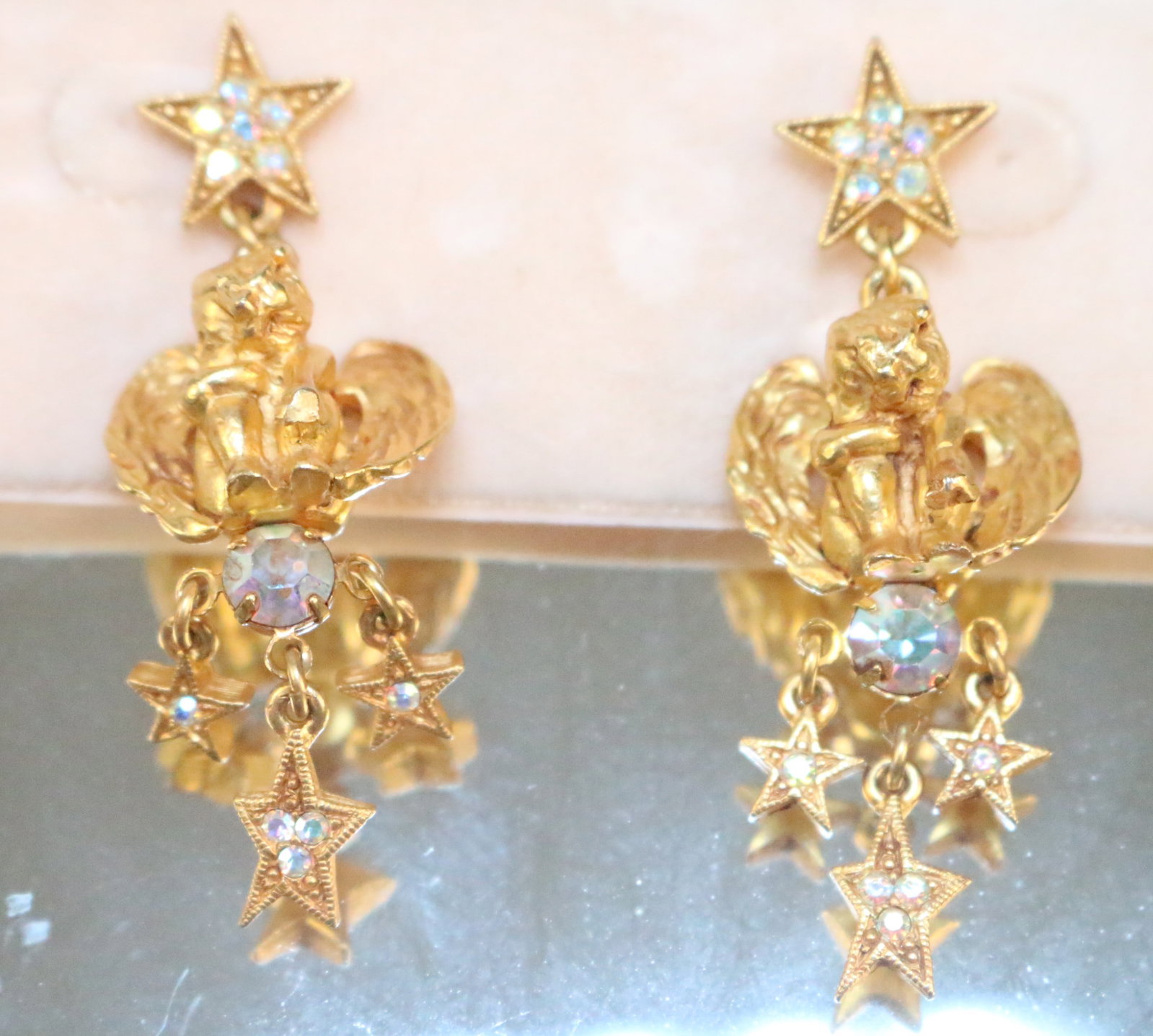 New Vintage Kirks Folly Angel Cherub Star Pierced earrings on Card: Stamped: Kirks Folly. On the Pink Card NEW YORK Made in the USA. Side sitting gold tone cherubs with angel wings. Crystal star posts, star and crystal dangle. DIMENSIONS: 2-1/4" long x 3/4" wide