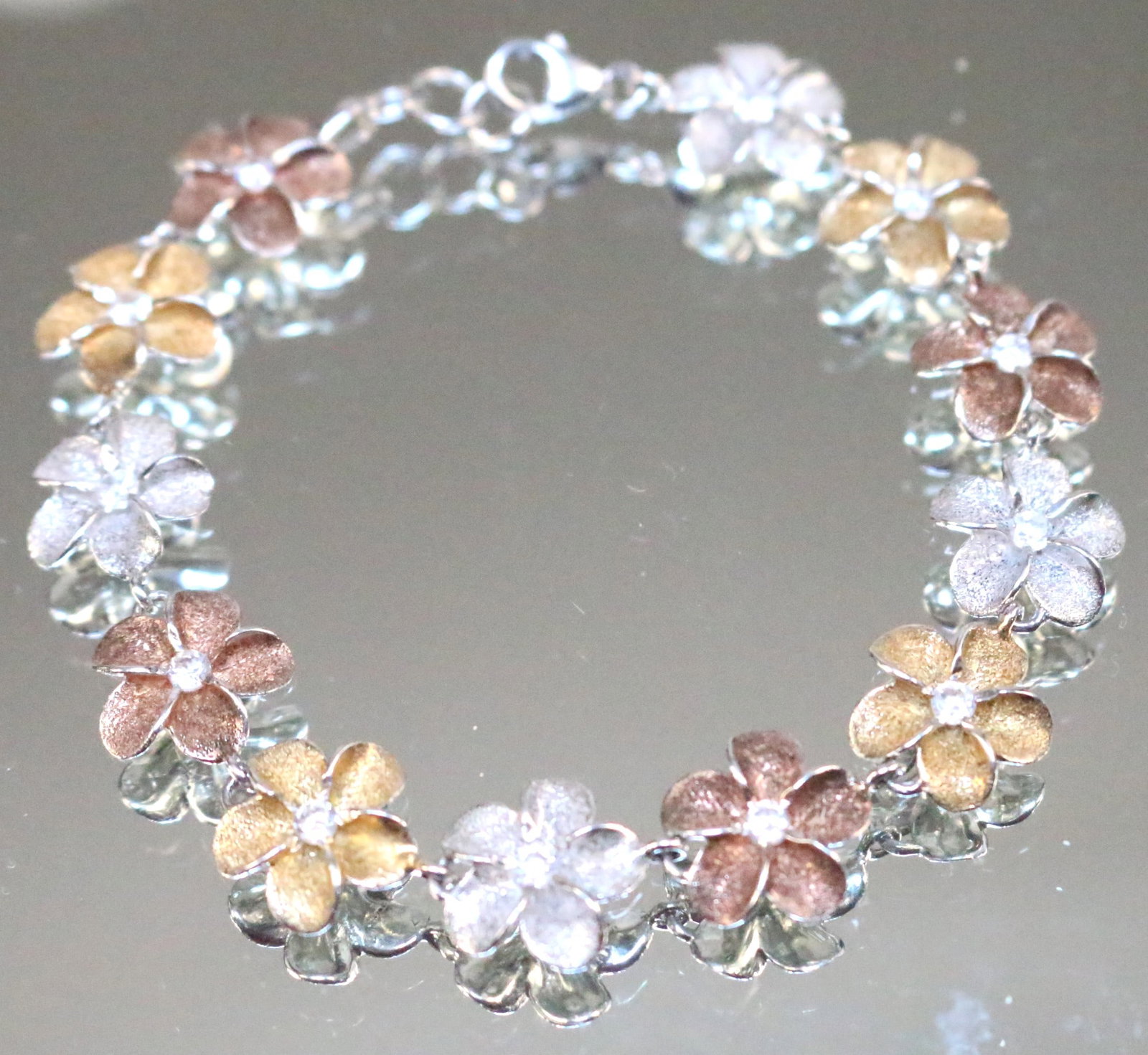 Kabana Sterling Silver tri color Plumeria Bracelet: STAMPED: K 925. DETAILS: Beautiful 3 color plumeria in silver, gold and copper with clear crystal centers. Matches pendant in LOT 247. DIMENSION: &" long with 1/2" flowers. WEIGHT: 9.2 grams.