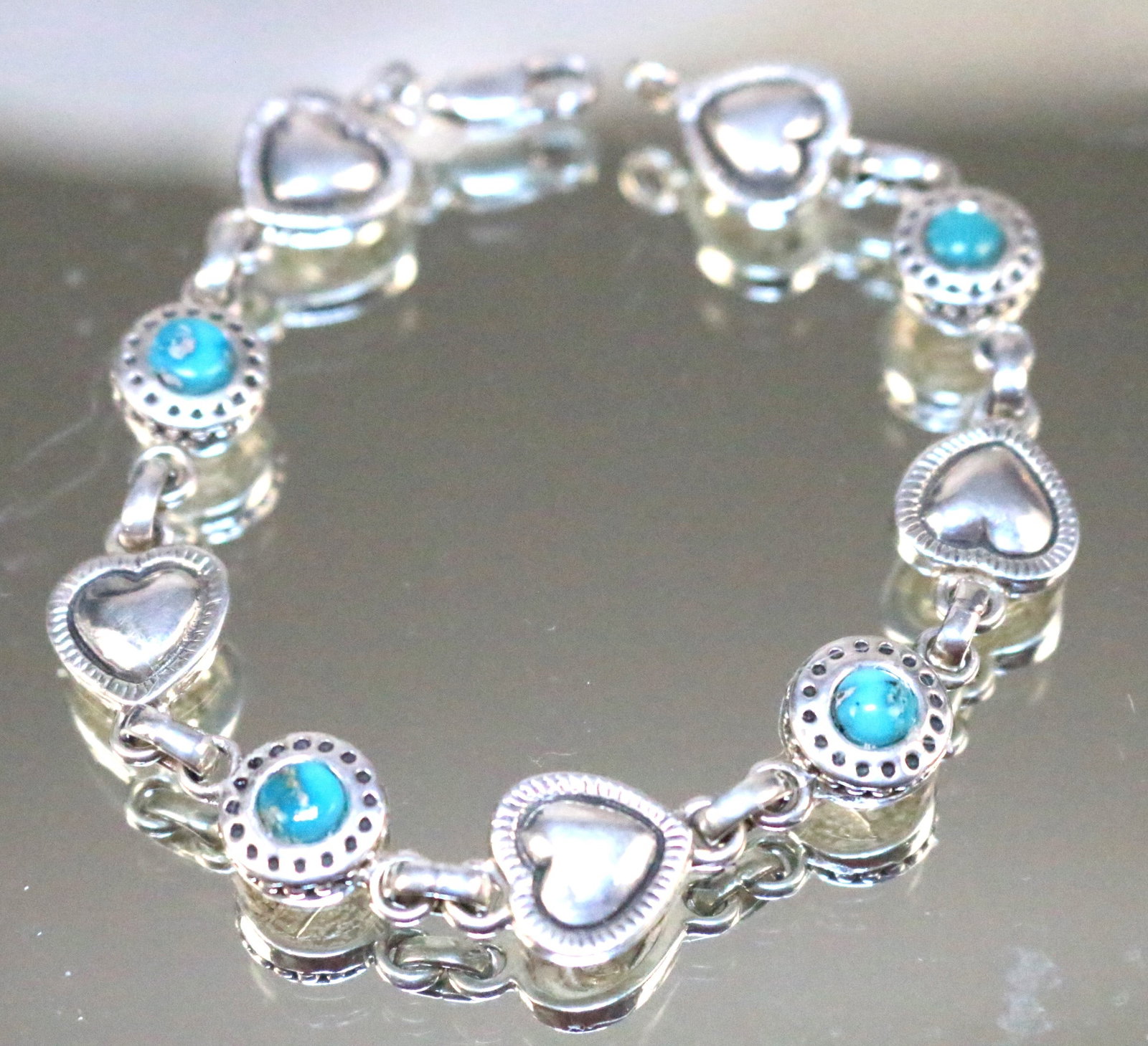 Carol Felley Sterling Silver Heart turquoise bracelet: STAMPED: CF Logo STERLING. DETAILS: Beautiful shiny silver alternating detailed hearts with embossed border and round turquoise in a raised open filigree setting. Lobster clasp closure. DIMENSION: 7.5