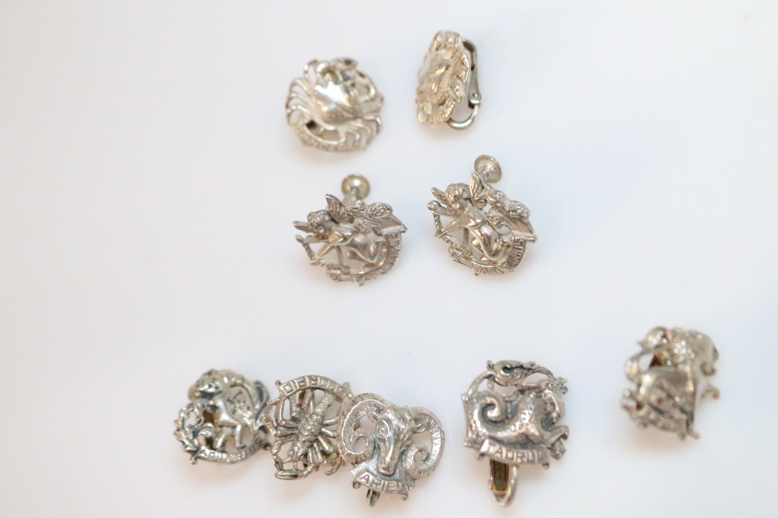 NEW OLD STOCK Sterling Silver CINI Zodiac Earrings 9 pieces.: SIGNED: Sterling by CINI. Sagittarius, Cancer, Aquarius, Scorpio, Aries, Taurus, Leo. DETAILS: 2 complete pair Sagittarius screw back earrings & Cancer clip back earrings. Aquarius, Scorpio, Aries, Ta