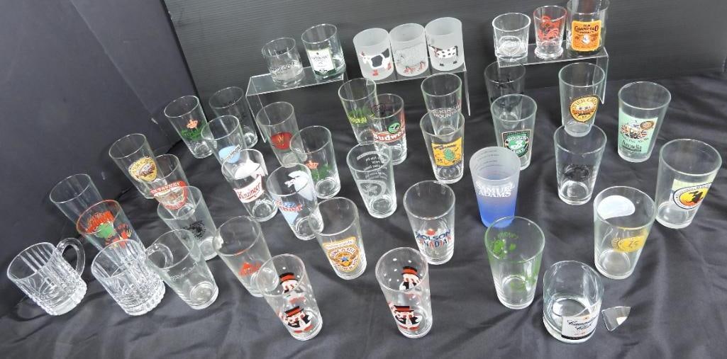 Lot of 43 beverage barware glasses advertising: 43 Various glass drinkware featuring several well known alcohol logos such as Samuel Adams, Blue Moon, and Budweiser; There is a Canadian club whiskey glass that has a substantial break by its rim