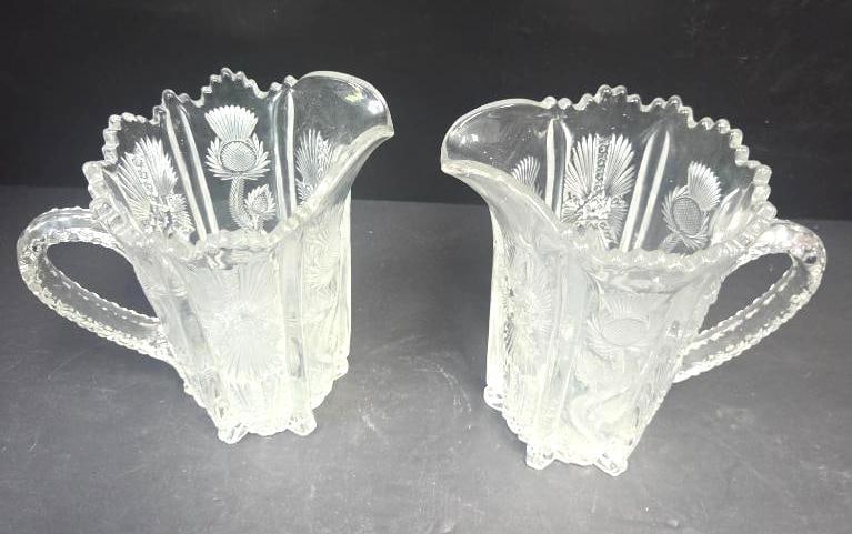 Pair of Pressed Glass Thistle Pattern Pitchers: Matching pair of small pitchers/creamers, thistle pattern body, pinched spout, applied handle, scalloped rim, footless flared base. Approx. 4.5"H x 4"W each.