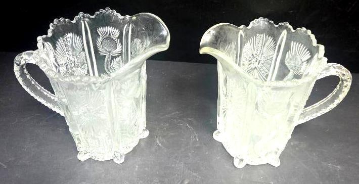 Pair of Pressed Glass Thistle Pattern Footed Pitchers: Matching pair of small pitchers/creamers, thistle pattern body, pinched spout, applied handle, scalloped rim, short scalloped feet (differs from Lot 113). Approx. 4.5"H x 4"W each.