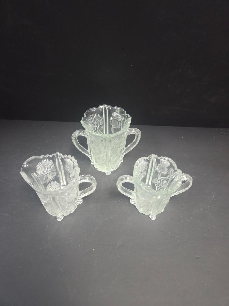 Mixed Grouping of Pressed Glass Creamers and Sugar: Small creamer, starburst pattern body, single applied handle, footed. Approx. 3.5"H x 3.5"W.Open sugar bowl, starburst pattern body, two applied handles, footed (taller than the two creamers).