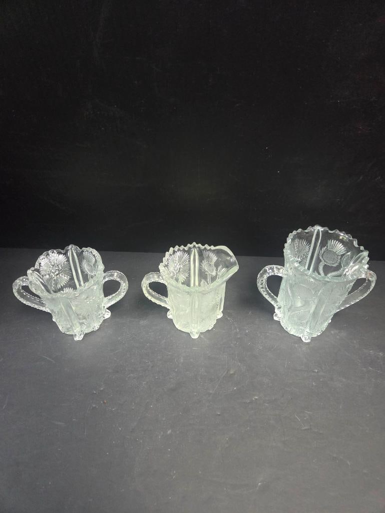 Mixed Grouping of Pressed Glass Creamers and Sugar: Small creamer, thistle pattern body, single applied handle, footed. Approx. 3.5"H x 3.5"W.Small creamer, thistle pattern body, single applied handle, footed, pinched spout (differs slightly in shape