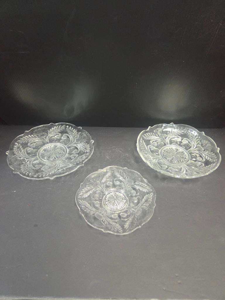 Grouping of Three Pressed Glass Fern Pattern Plates: Round plate, fern/leaf pattern with scalloped rim. Approx. 6.5"W.Round plate, matching fern/leaf pattern (matches item above). Approx. 6.5"W.Small quatrefoil (four-lobed) plate, floral/berry pattern,