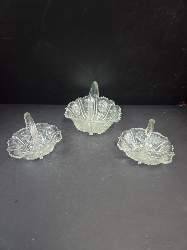 Grouping of Three Pressed Glass Thistle Pattern Baskets: Small basket, oval body, thistle pattern, applied swirl handle. Approx. 4"H x 4"W.Small basket, matching the item above. Approx. 4"H x 4"W.Larger basket, matching thistle pattern and swirl handle