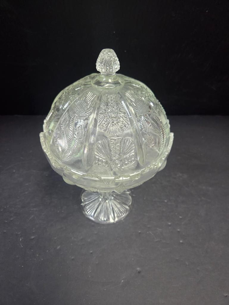 Pressed Glass Thistle Pattern Covered Candy Dish: Covered candy dish, domed lid with faceted teardrop finial, thistle and fern pattern body, scalloped rim, pedestal foot. Approx. 6.5"H x 5"W.