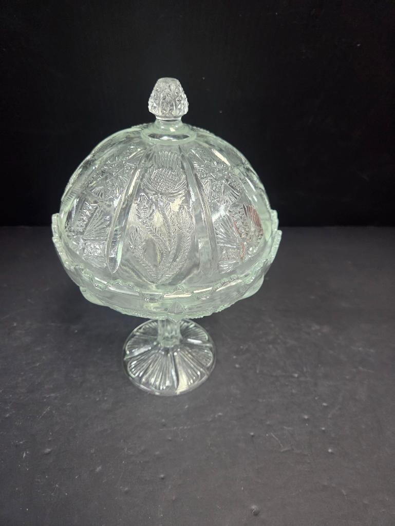 Pressed Glass Thistle Pattern Covered Candy Dish: Covered candy dish, domed lid with faceted teardrop finial, thistle and fern pattern body, scalloped rim, pedestal foot (closely matches Lot 149). Approx. 6.5"H x 5"W.