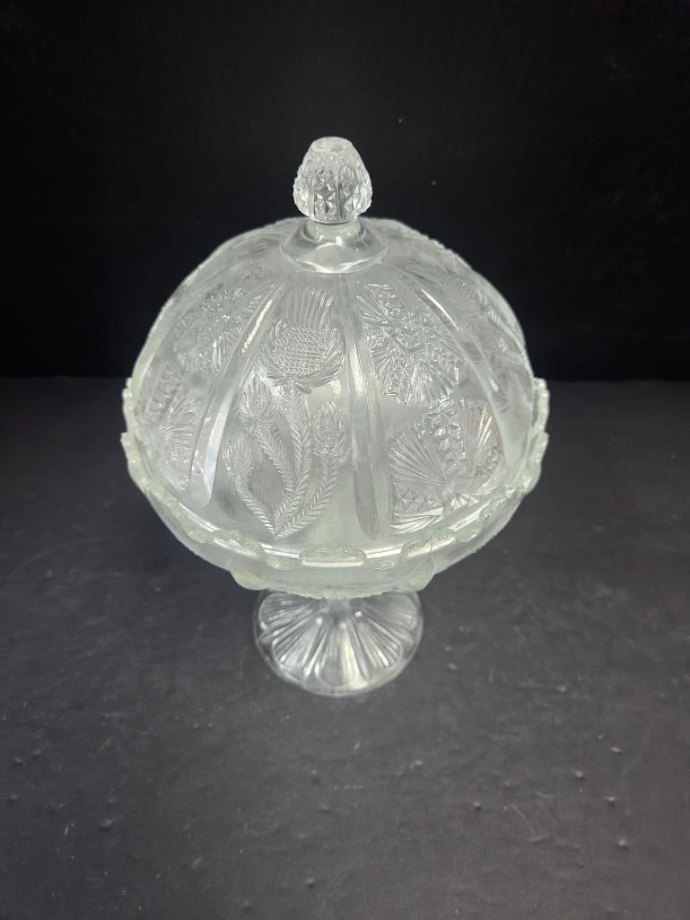 Pressed Glass Thistle Pattern Covered Candy Dish: Covered candy dish, domed lid with faceted teardrop finial, thistle and fern pattern body, scalloped rim, pedestal foot (closely matches Lots 149 and 150). Approx. 6.5"H x 5"W.