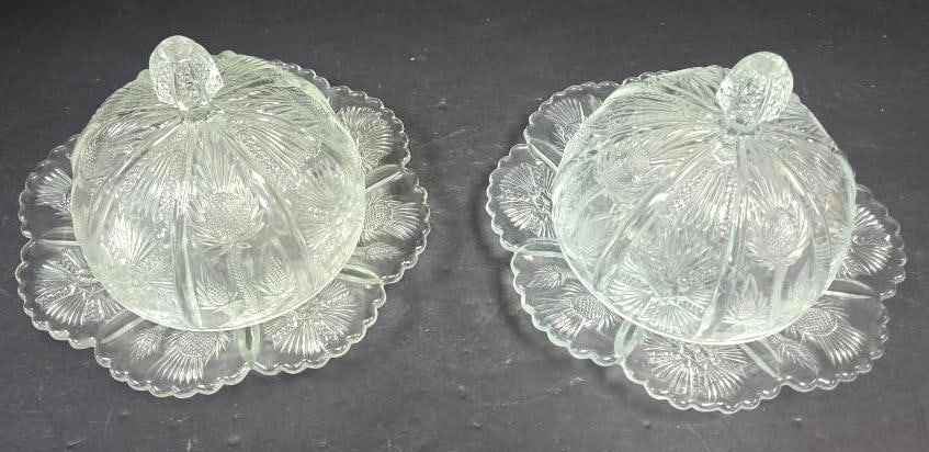 Pair of Pressed Glass Thistle Pattern Covered Cheese/Butter Dishes on Underplate: Matching pair of domed covered dishes on a round scalloped underplate, thistle and fern pattern, faceted teardrop finial. Approx. 6"H x 8"W each.