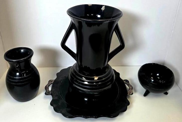 Grouping of Four Black Glass Vases, Tray, and Bowl: Small vase, black glass, ribbed neck. Approx. 5"H.Art deco-style trumpet vase, black glass, angular diamond-shaped handles, tiered ringed base. Approx. 9"H.Scalloped tray/underplate, black glass, twig