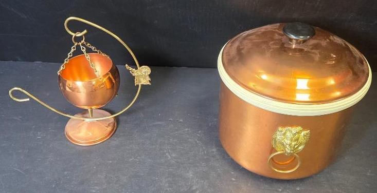 Copper Warming Stand and Lidded Pot: Hanging copper warming pot on a brass stand with chain suspension. Approx. 10"H.Copper lidded pot with brass lion-head ring handles, cream-colored rim trim. Approx. 7"H x 8"W.
