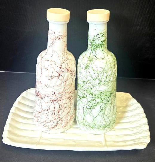 Painted Glass Bottles on Ceramic Tray: Glass bottle with cream-colored lid, decorated with a red thread/drizzle design over white enamel. Approx. 9"H.Matching glass bottle, decorated with a green thread/drizzle design (color differs from