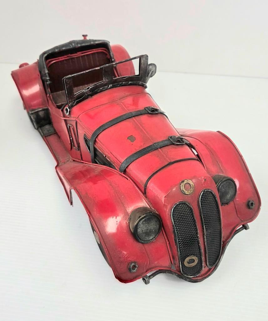 Distressed-Finish Decorative Tin Model Roadster: Decorative red painted-tin vintage roadster with intentionally weathered/distressed finish, black leather-look straps across the hood, twin oval mesh grilles (BMW 328-style), open cockpit with dark