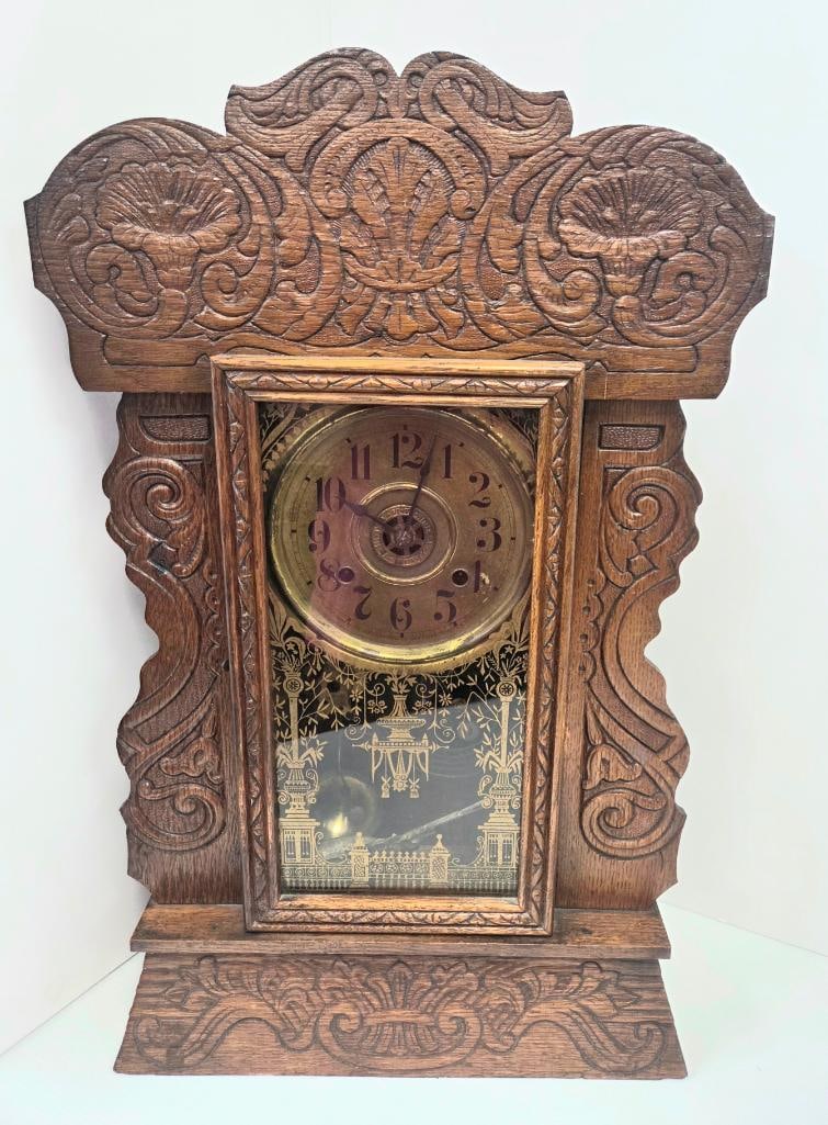 Carved Oak Gingerbread Mantel Clock: Antique carved oak "gingerbread" style mantel clock, ornate crest with shell and scroll carving, brass-tone dial with Arabic numerals, glazed door with gilt-decorated lower glass panel, visible pendul