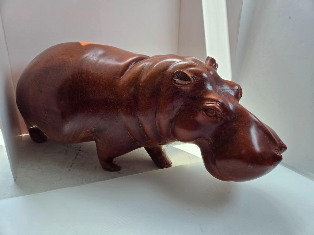 Carved Wood Hippopotamus Figurine: Hand-carved wood figurine of a hippopotamus, polished reddish-brown finish, naturalistic detailing of ears, eyes, and mouth, minor age crack along the back, approx. 14" L x 5" W x 7" H.