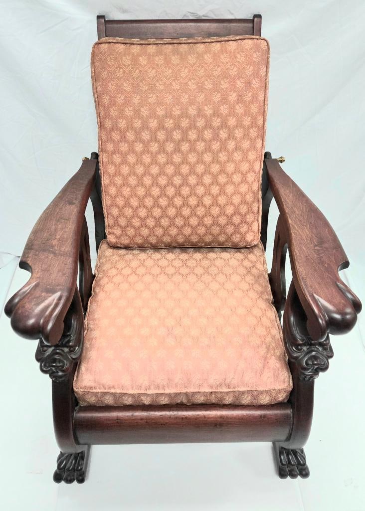 Victorian Carved Platform Rocker with Lion-Head Arms: Antique dark wood Victorian-style platform rocking chair, carved lion-head arm terminals with paw feet, brass locking/pivot hardware at the sides, salmon/pink damask upholstered back and seat
