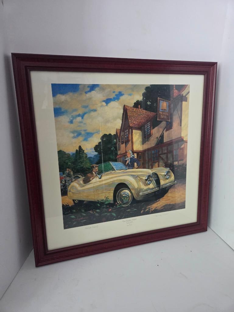 "The Golden Years" Artist Proof Print by Barry Rowe: Framed artist proof print titled "The Golden Years, 50 Years of the Jaguar XK120" depicting a cream Jaguar XK120 roadster with two figures outside the "Ye Olde Bell" inn, cherry-tone frame with cream
