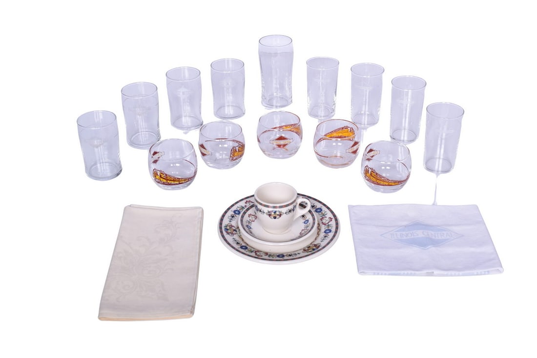 Nineteen Pieces of Illinois Central Railroad Glassware, China Plate, and Linen Napkins: A collection of dining car items for the Illinois Central Railroad including five 2 3/4" roly poly style drinking glasses, side marked with the diamond logo and locomotive graphic in red and yellow en