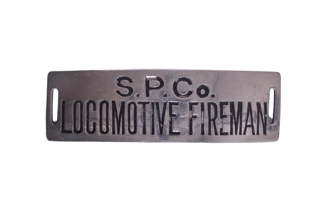 Southern Pacific Company Railroad Locomotive Fireman Cap Badge: A nickel plated rectangular cap badge for the Southern Pacific Company Railroad with black enameled letters and slotted ends measuring 3 3/8" x 1 1/16". Manufactured by Irvine & Jachens 1027. The badg