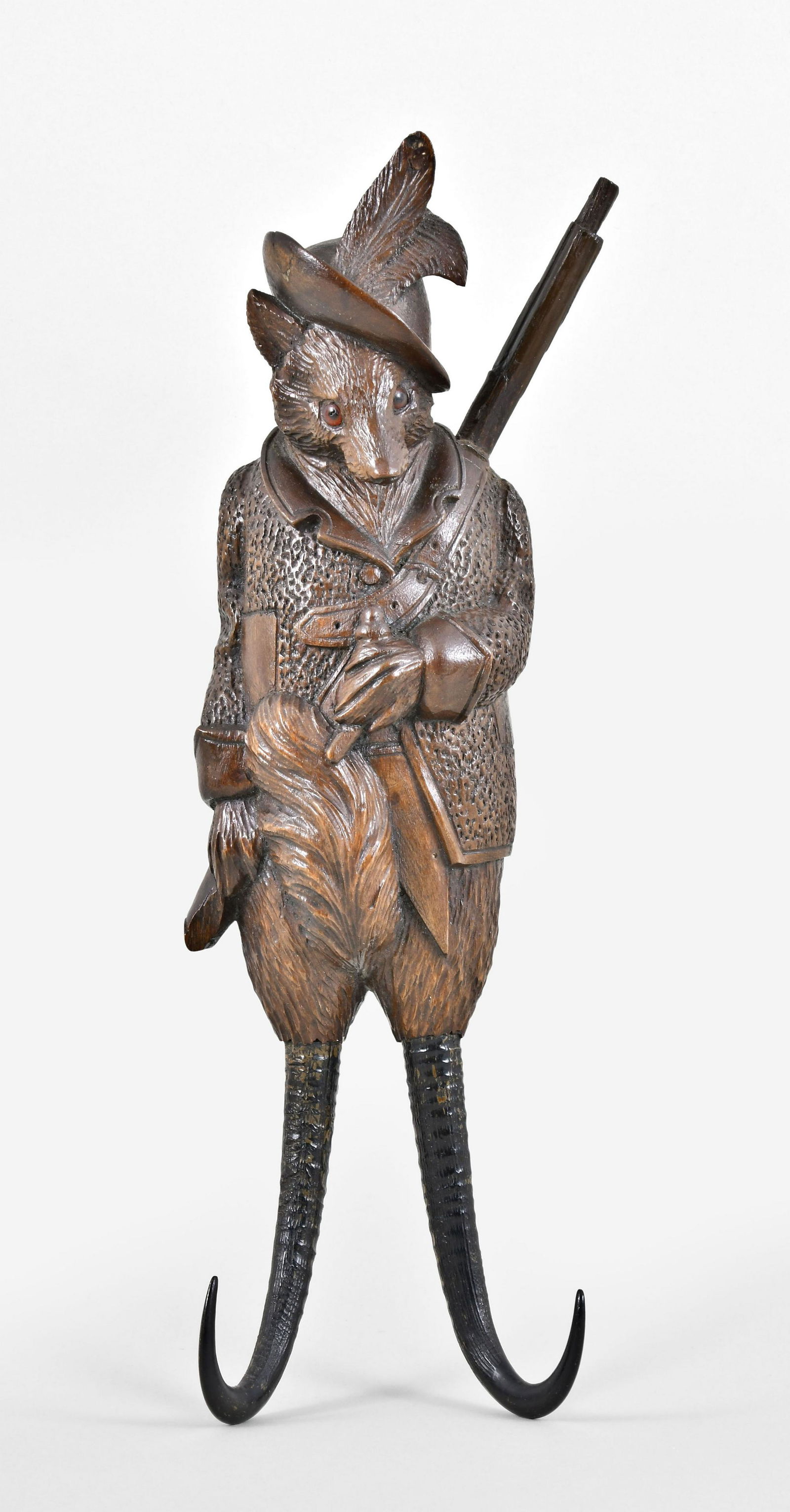 A Black Forest carved musical fox form crop hook: Switzerland, a Black Forest carved musical fox form crop hook, the figure with glass eyes, feathered hat, coat, a rifle across his back, and fox call in his left paw, his legs ending in chamois horn h