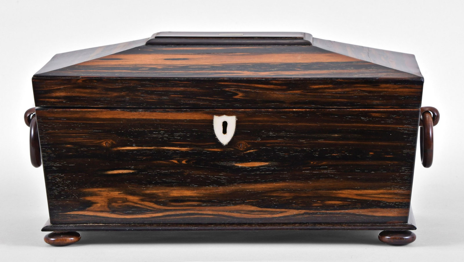 A good 19th century English coromandel tea caddy: England, a good 19th century English coromandel tea caddy, of sarcophagus form, on compressed ball feet and with wooden ring handles and shield shaped escutcheon, the cover lined with gilt stamped bur