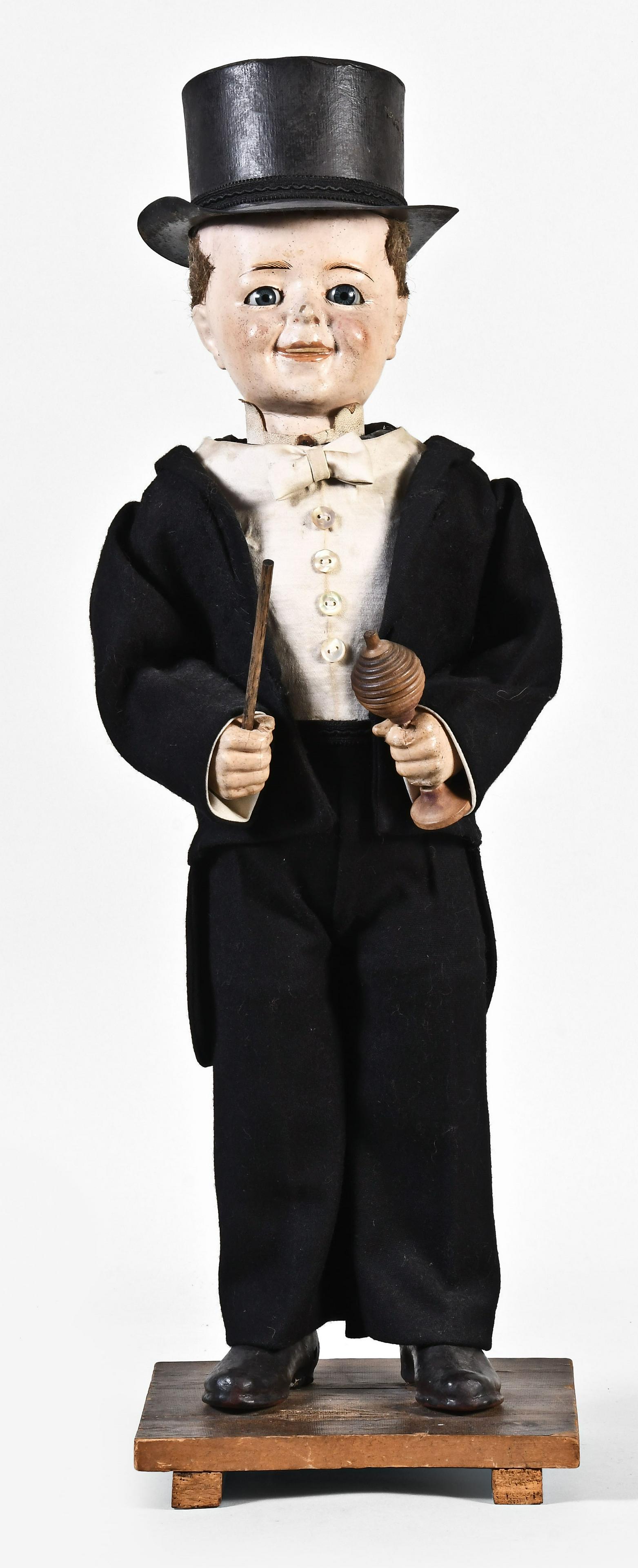 An early 20th century German clockwork Magician nodder: Germany, an early 20th century clockwork "Magician" nodder, the papier mache and composition figure with tuxedo, top hat, and blue glass eyes, his right hand with wand, and his left with ball and vase