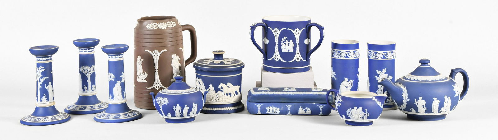 A lot of Wedgwood and Adams blue and brown jasper wares: A lot of Wedgwood and Adams blue and brown jasper wares, including three candlesticks, a loving cup, a cream pot, a tea pot, a sugar bowl, a butter dish, two small cylindrical vases, a covered jar, an
