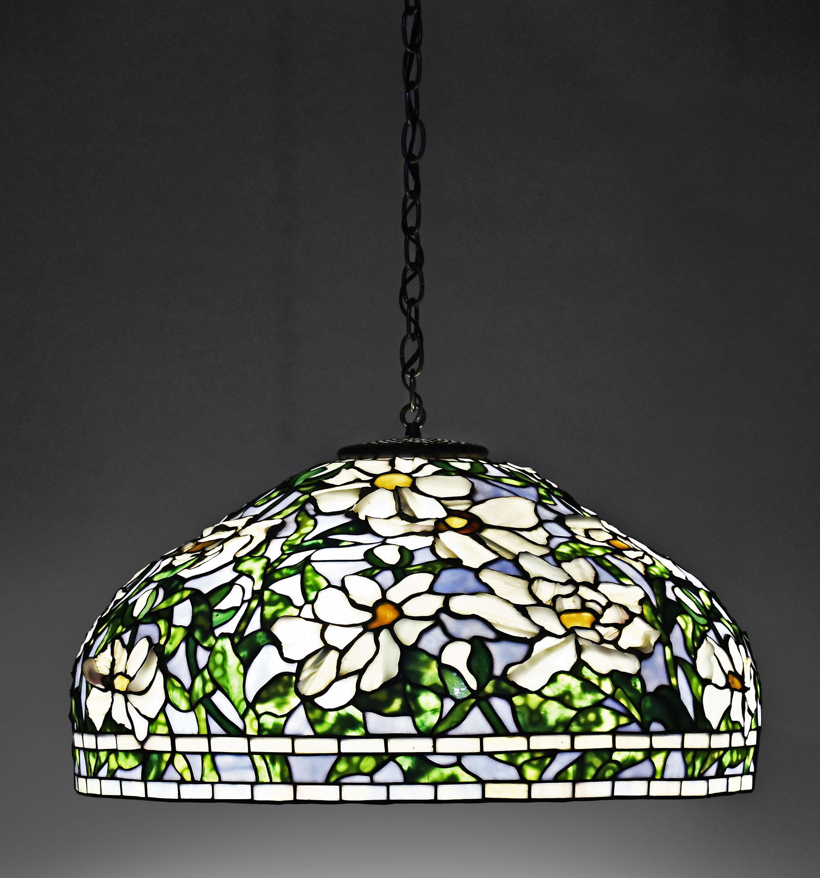 A decorative late 20th century hanging slag glass lamp shade: A large, decorative late 20th century hanging leaded slag glass lamp shade, the domed construct decorated with white flowers and green foliage, on a light blue background, the flowers assembled from w