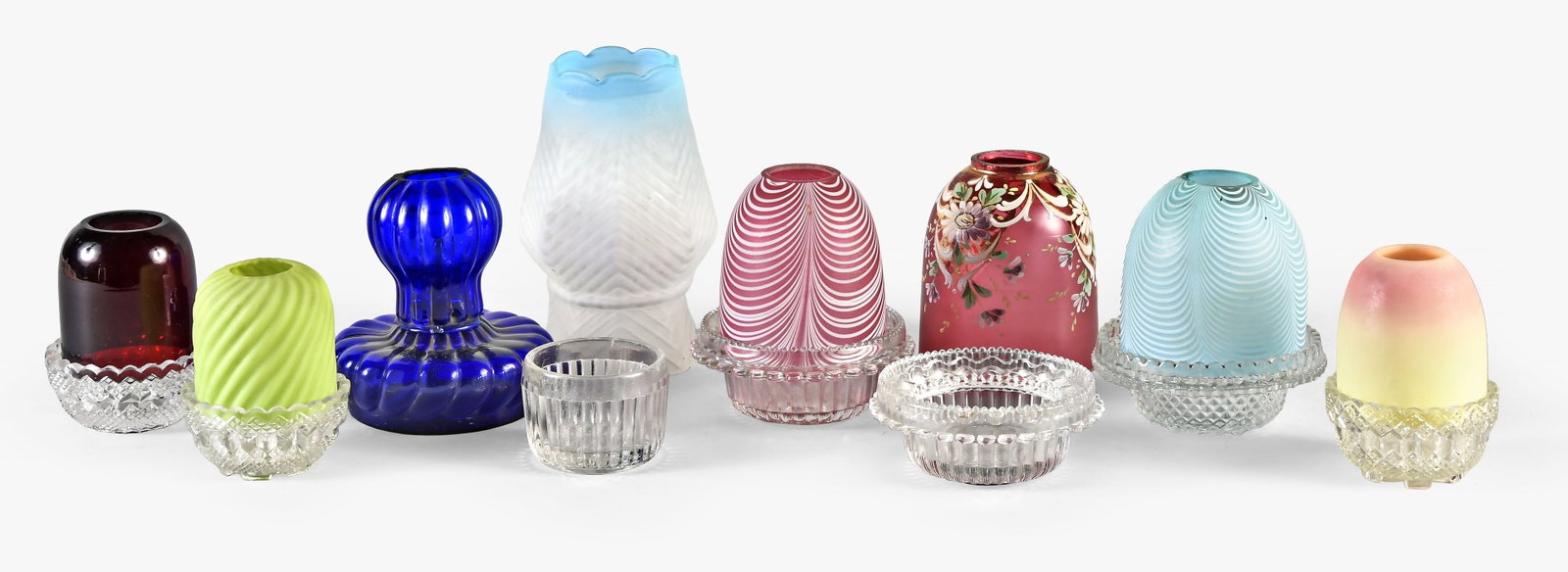 A lot of Clarke fairy lamps and fairy lamp parts: Clarkes Pyramid and Fairy Lamp Co., London, a lot of fairy lamps and fairy lamp parts, the shades including blue and red nailsea, a chartreuse twisted reed, a Burmese, and one in ruby red, together wi