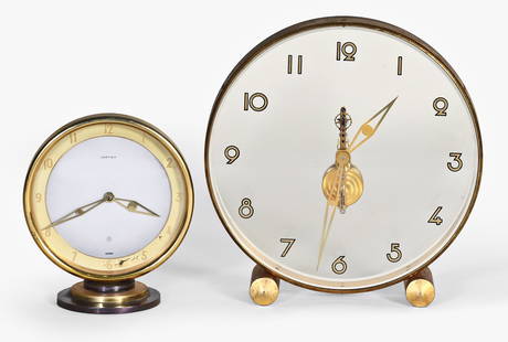 A lot of two desk or table clocks by LeCoultre and Cartier: 2 (Two) desk or table clocks, the first by LeCoultre for Cartier, round gilt brass case on cylinder feet, arabic numeral 7.5 inch transparent dial, the back also transparent and with 8 day, 16 jewel c