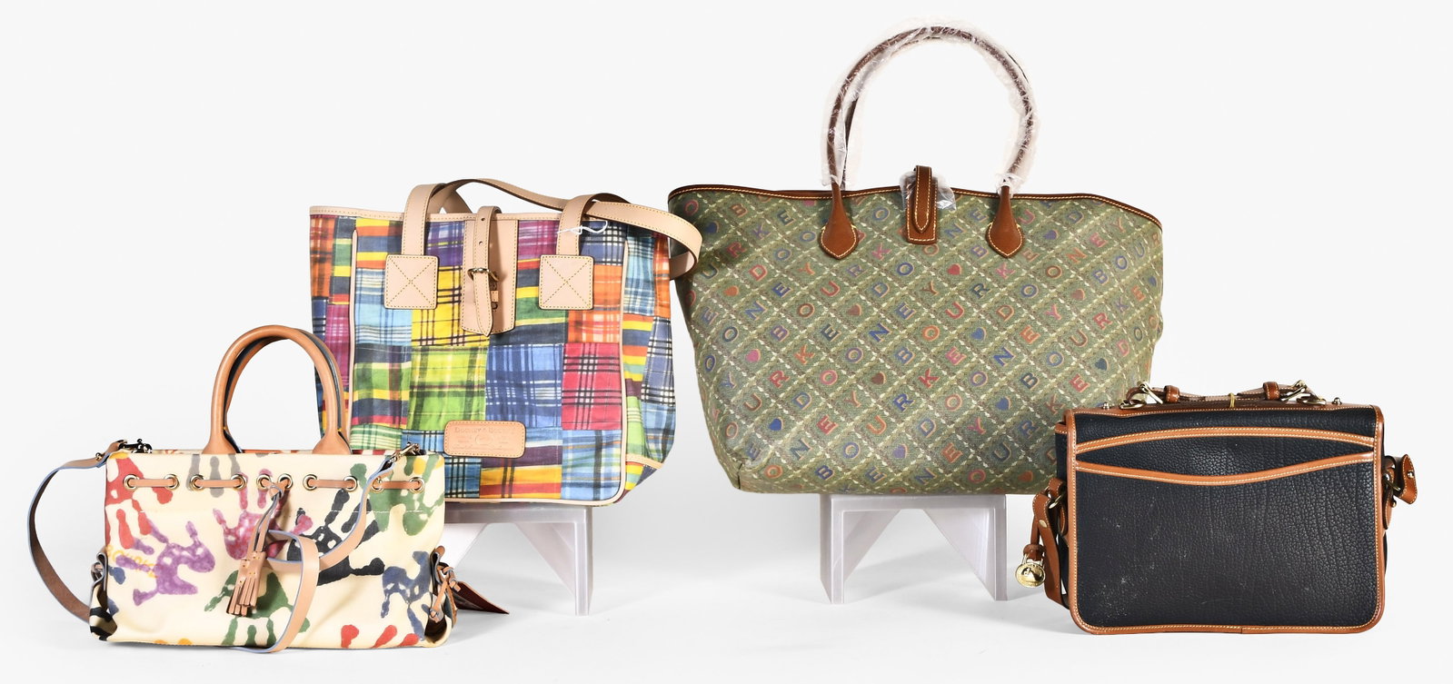 A lot of four late 20th - early 21st century Dooney & Bourke bags: 4 (Four) late 20th - early 21st century Dooney & Bourke bags including a large tote with "Dooney & Bourke" spelled out in repeating diagonals across the surface, with sales tag and protective wrap, a 