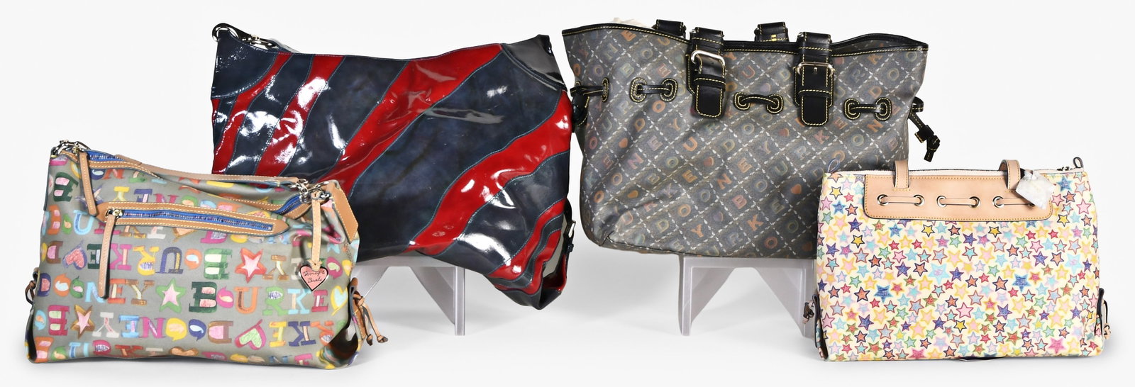 A lot of four late 20th - early 21st century Dooney & Bourke bags: 4 (Four) late 20th - early 21st century Dooney & Bourke bags including a large tote with glossy diagonal red and blue stripes, a large tote with "Dooney & Bourke" spelled out in repeating diagonals ac
