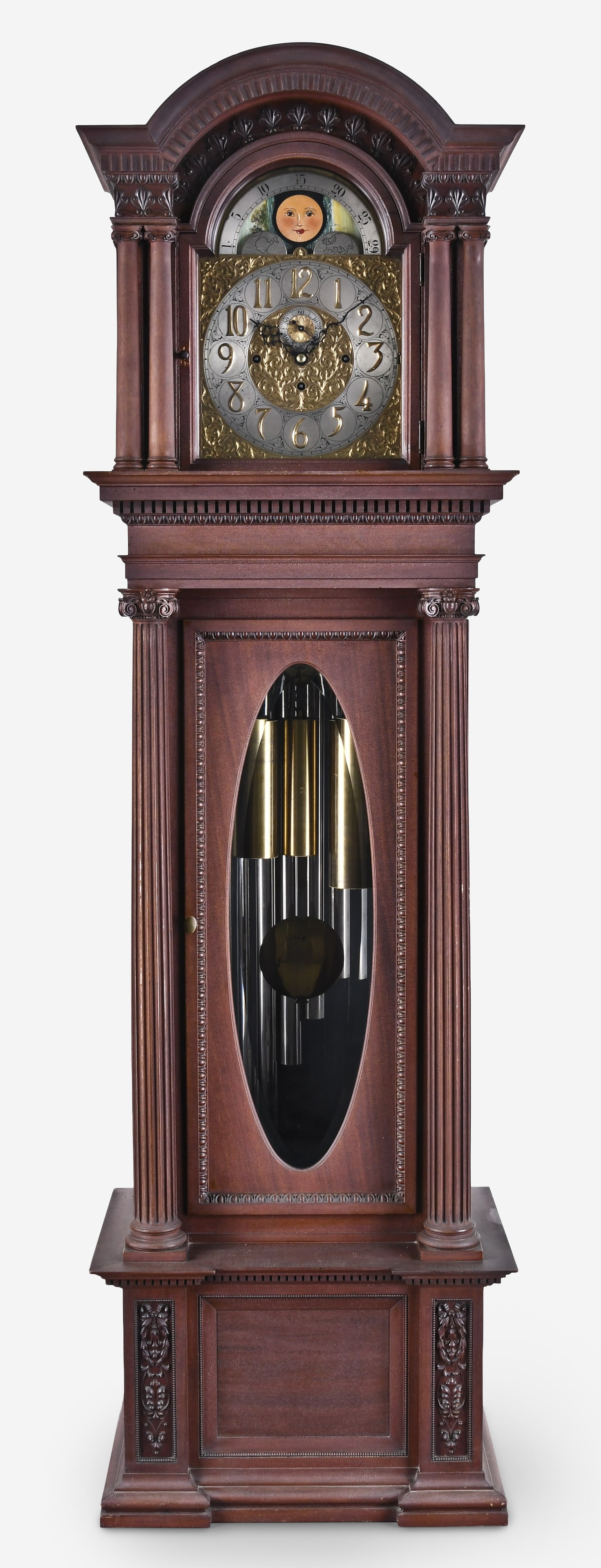 An Elliott chiming hall clock: J.J. Elliott, London chiming hall clock in a carved mahogany case with arched top with dentil molding and foliate carvings, four fully turned columns with carved capitals and bases flanking the hood