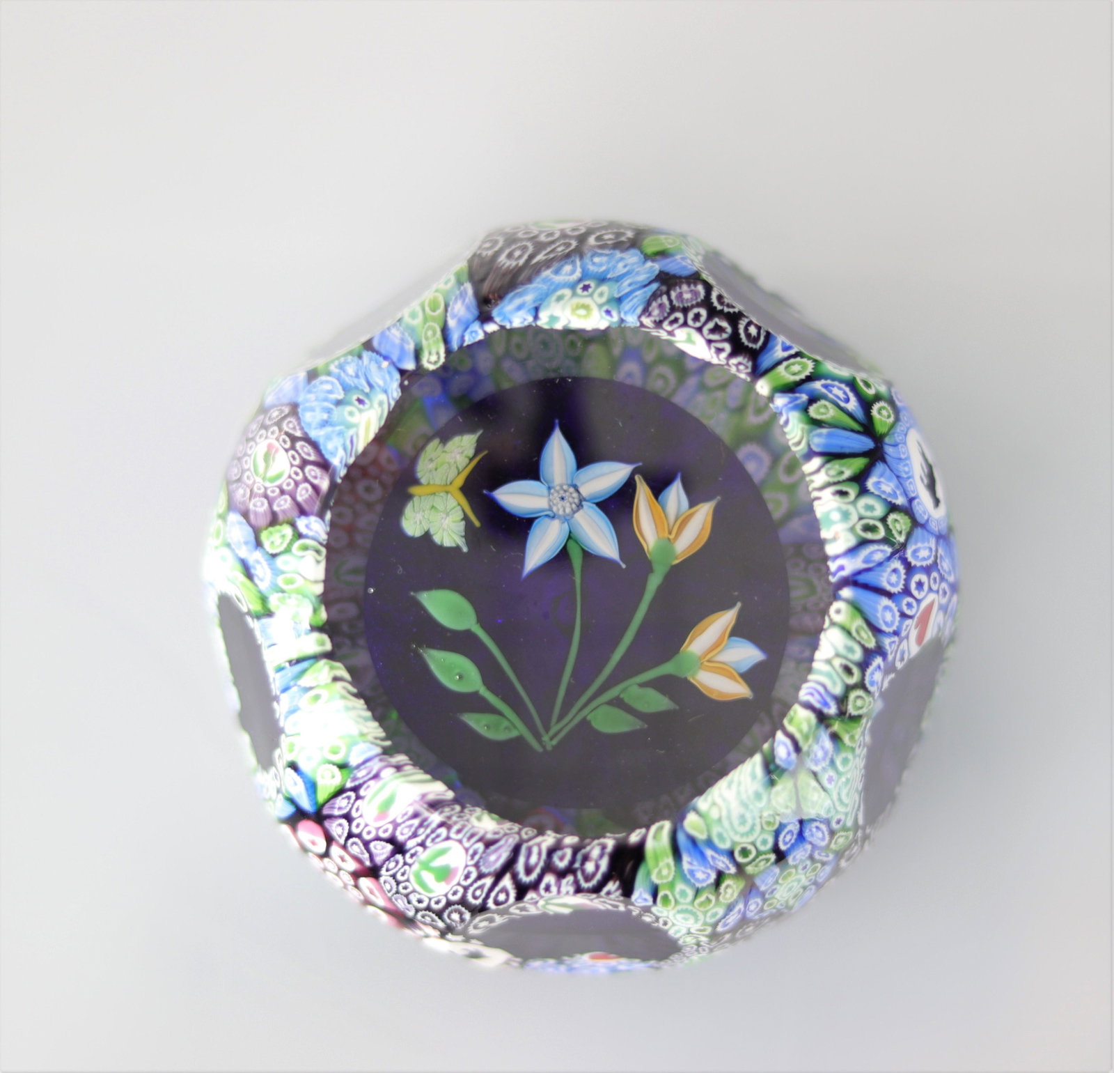 John Deacons paperweight 2003, overlay with canes on black cushion, 3 flowers and 1 butterfly: John Deacons paperweight 2003, overlay with canes on black cushion, 3 flowers and 1 butterfly - Weight: 650 g - Sizes: H=55mm D=85mm - Condition: good condition - Author / artist: John Deacons