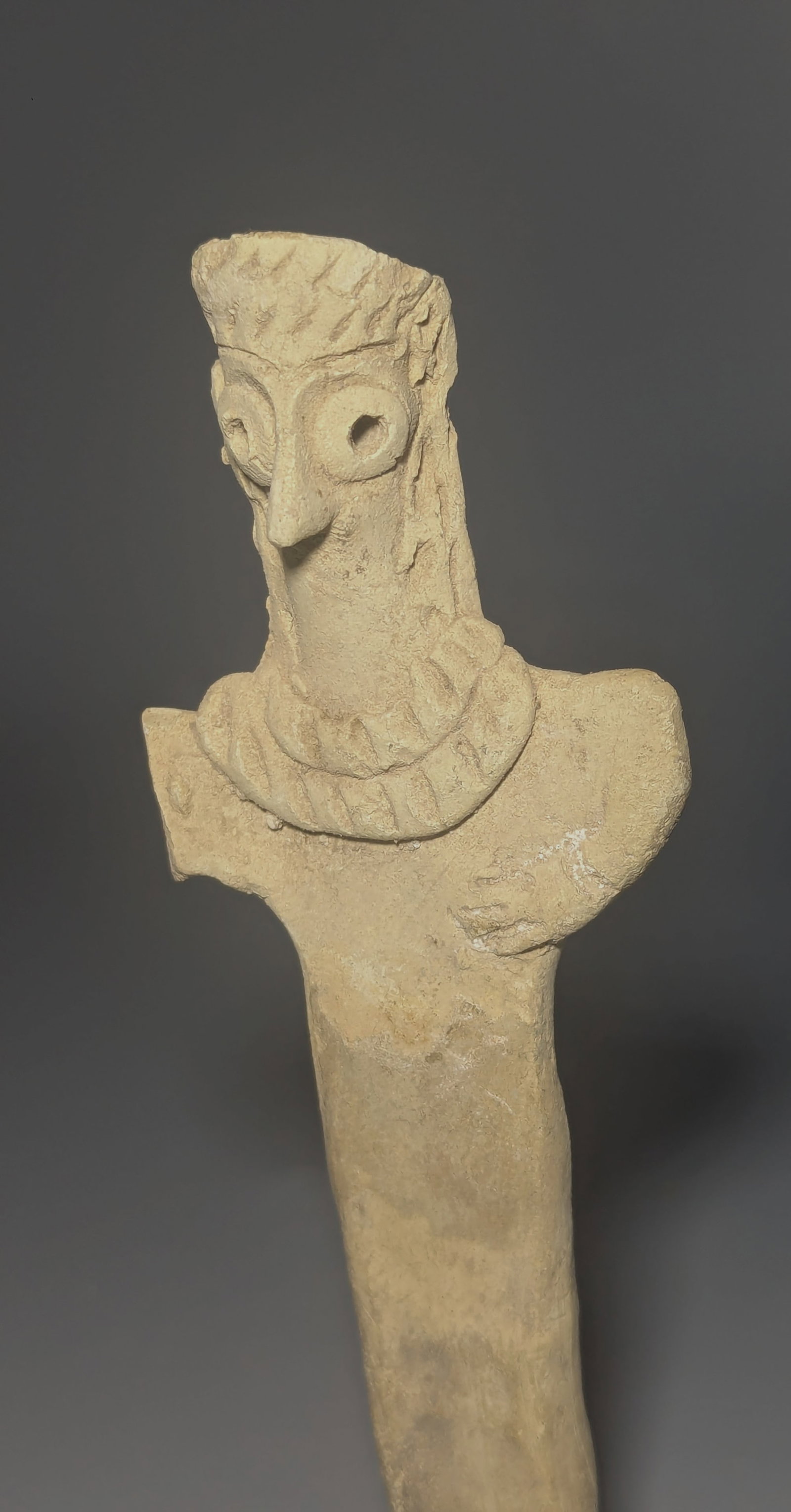 Syro-Hittite Terracotta Bird-Faced Female Idol: Syro-Hittite hand-modeled terracotta female idol of highly stylized form, featuring prominent pierced spectacle eyes, a projecting bird-like nose, incised coiffure or headdress, broad applied collar, 