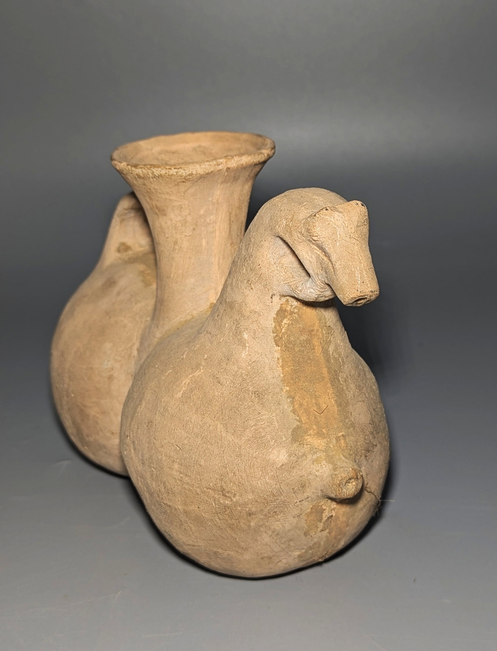 Near Eastern-Style Terracotta Zoomorphic Double Vessel: A terracotta double-bodied vessel modeled with a stylized animal head, tall flaring neck, and loop handle, after ancient Near Eastern prototypes. Decorative reproduction. Size: Approximately 8 in. lon