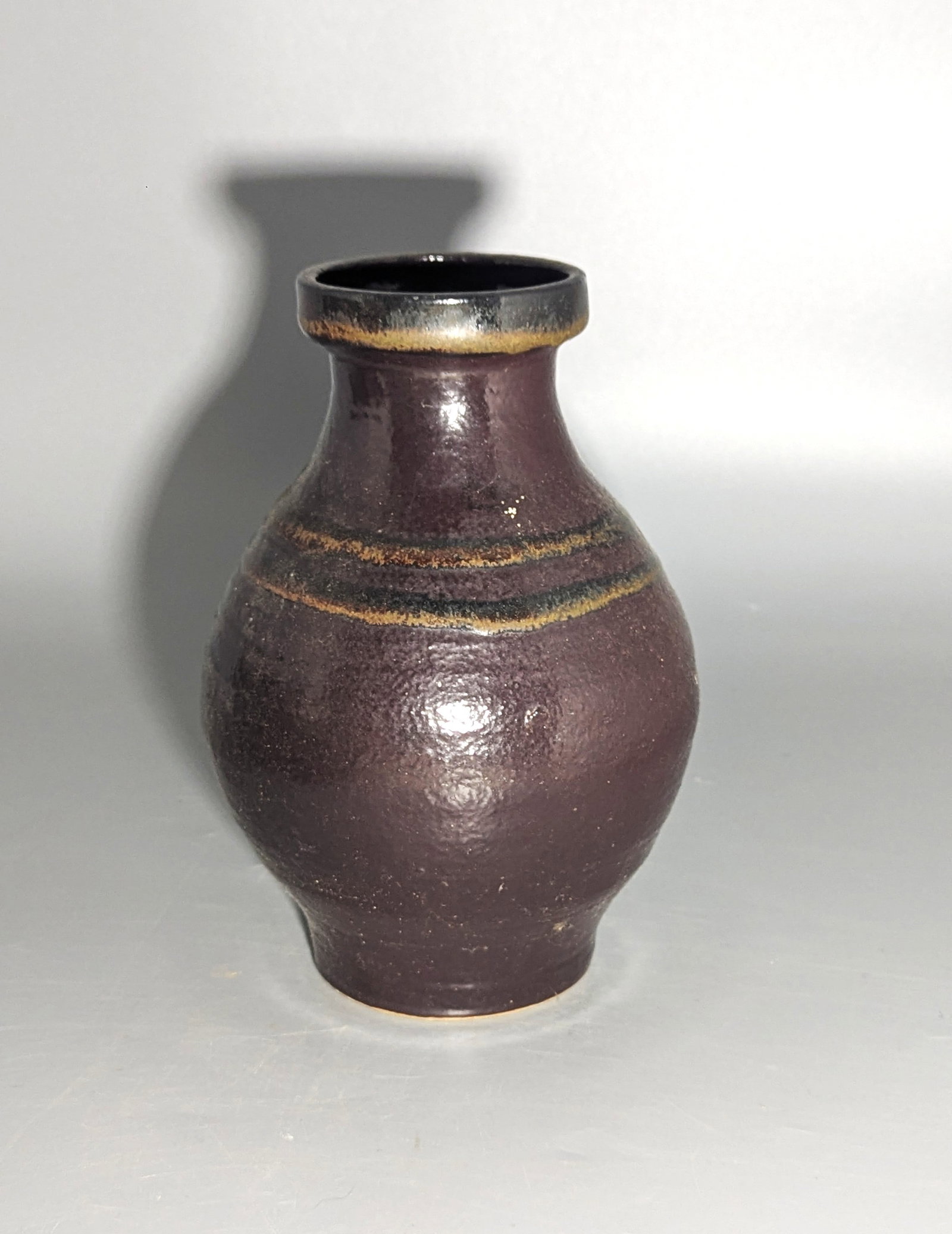 Japanese Tenmoku-Glazed Studio Pottery Vase: Japanese wheel-thrown stoneware vase of rounded form, covered in a deep black-brown Tenmoku glaze breaking to warm ochre along the lip and horizontal bands. Unmarked, 20th century. Size: 7.5 in. high.