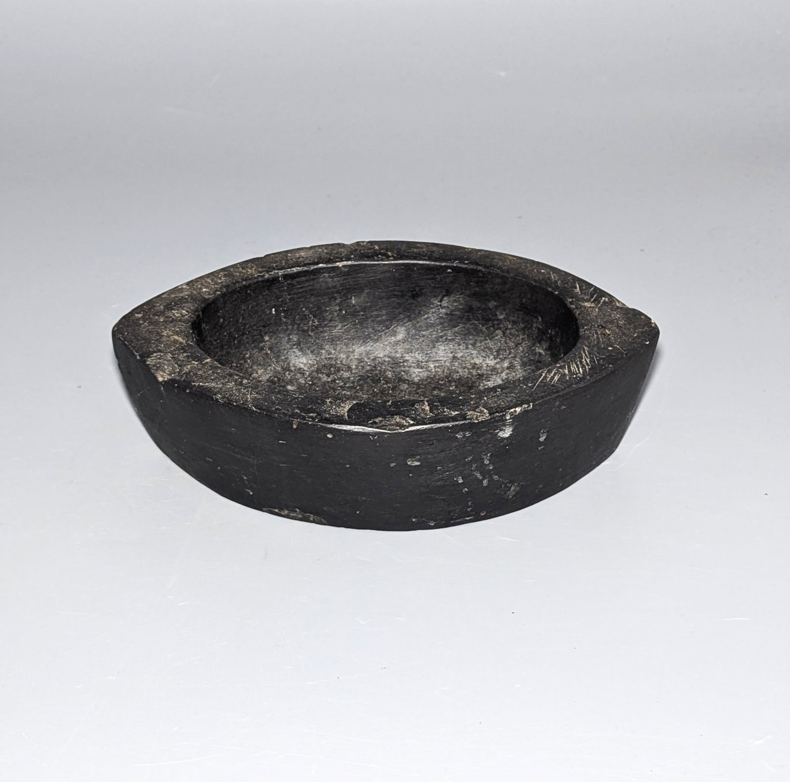Antique Indian Hand-Carved Black Stone Kharal Bowl: A substantial hand-carved Indian black stone kharal of elongated boat-shaped form, deeply hollowed to the center with a thick angular rim and solid rounded exterior. Vessels of this type were traditio