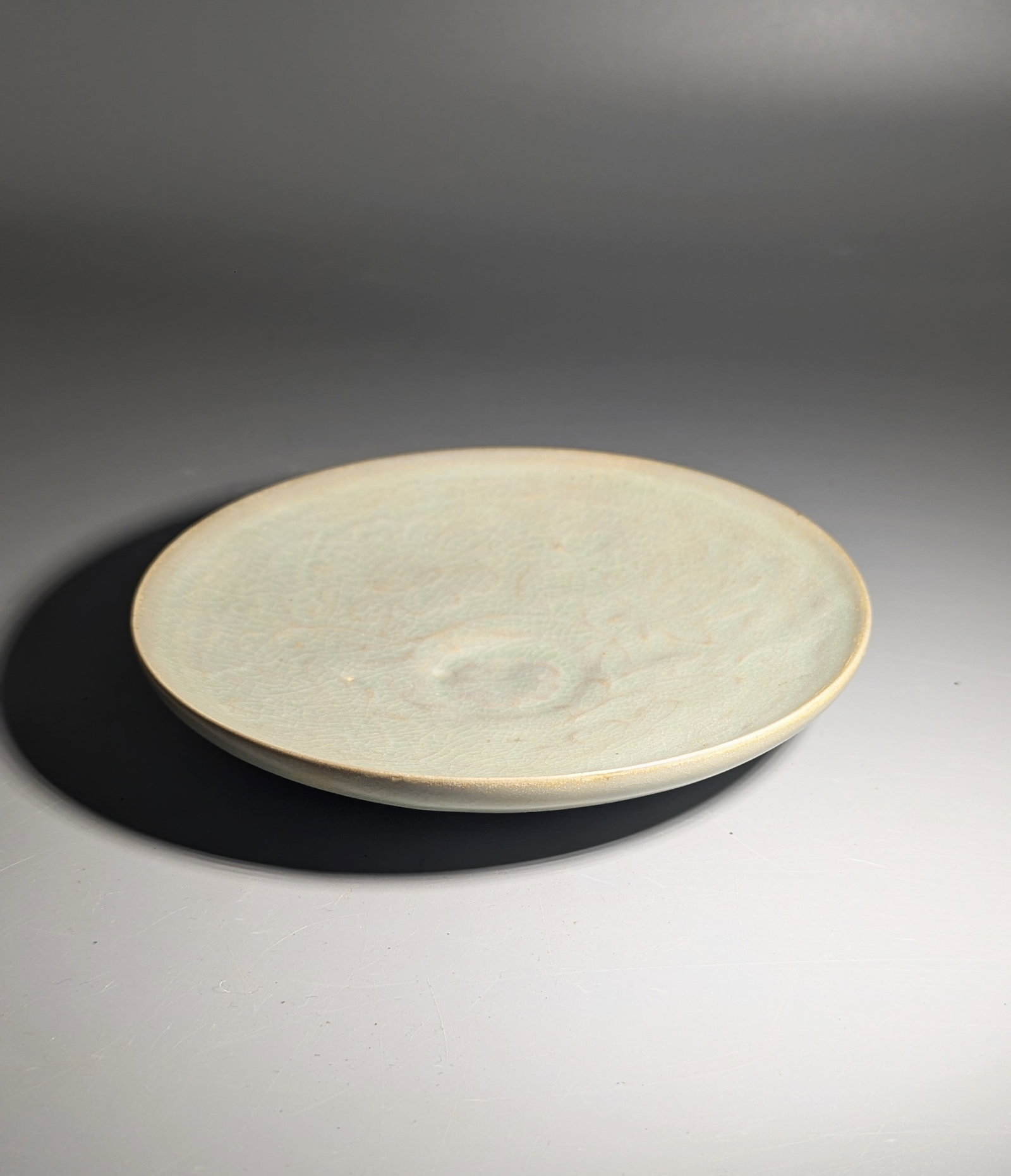 Korean Celadon Incised Floral Dish: A finely potted Korean celadon-glazed stoneware dish, the shallow interior delicately incised with a floral and foliate design beneath a soft gray-green glaze with an extensive network of fine crackle