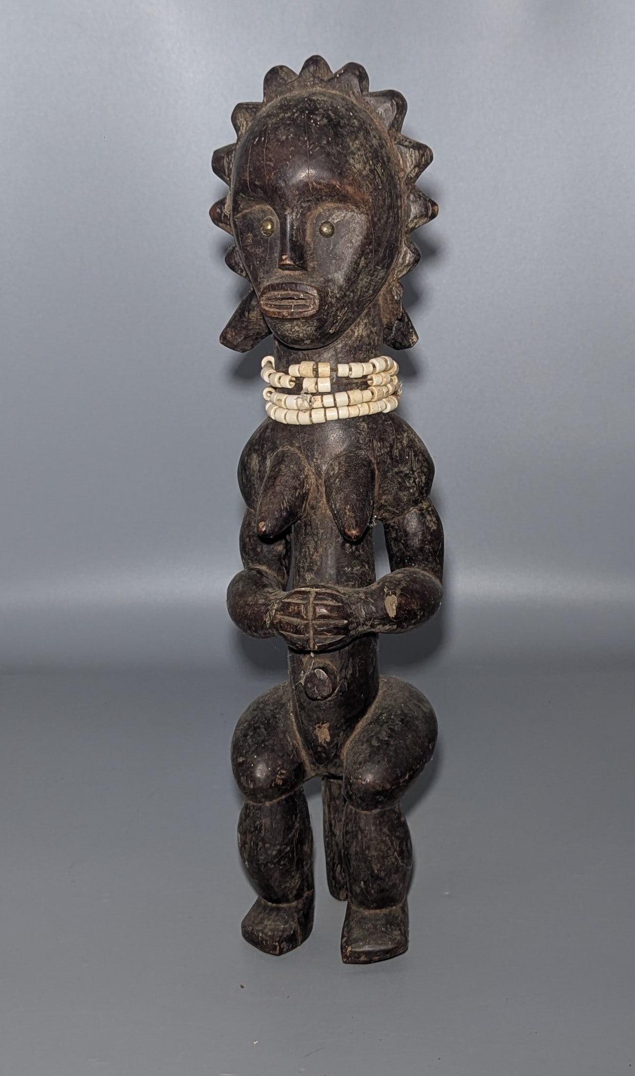 Fang Carved Wood Female Reliquary Figure, Gabon: A carved wood female figure attributed to the Fang peoples of Gabon and the surrounding Equatorial African region, modeled standing with an enlarged rounded head, brass-inlaid eyes, projecting breasts