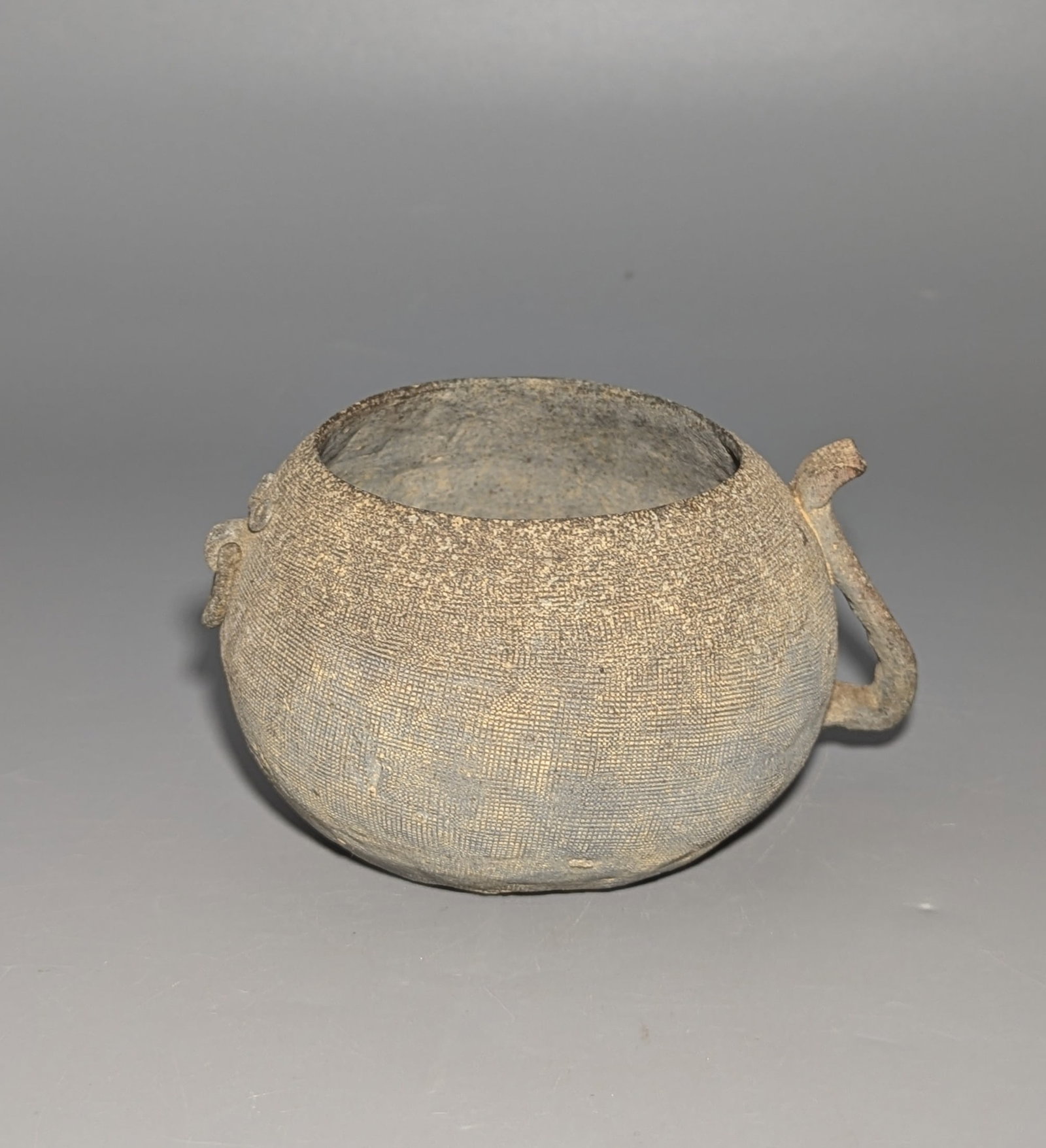 Chinese Impressed Gray Pottery Handled Vessel: An ancient Chinese gray pottery vessel attributed to the Eastern Zhou to Warring States period, 5th-3rd century BCE. The rounded body is densely covered with a remarkably fine impressed textile or cor