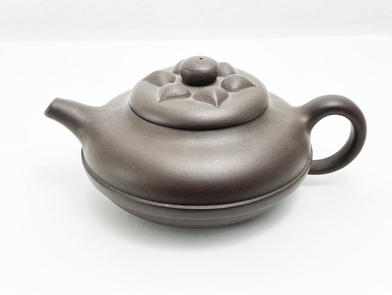 Chinese Yixing Clay Teapot: Chinese Yixing clay teapot with a flattened circular shape and petal motifs on the lid. Impressed mark on the undersides of pot. Two tiny hairline cracks on the inside rim. Dimensions: 6”W x 2.5