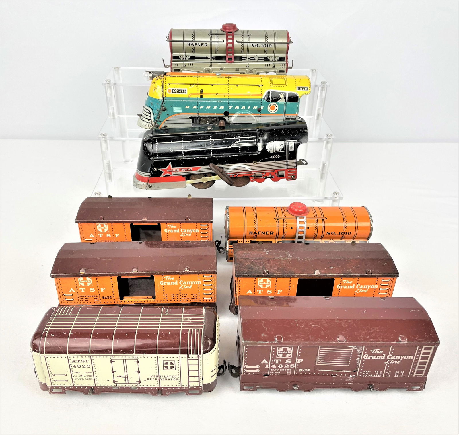 Group Early Hafner Engines & Train Cars: Group of nine (9) early vintage Hafner tin litho wind-up train engines and cars including two engines, two tankers and assorted box cars. Key is missing on one of the engines. Vintage wear throughout.