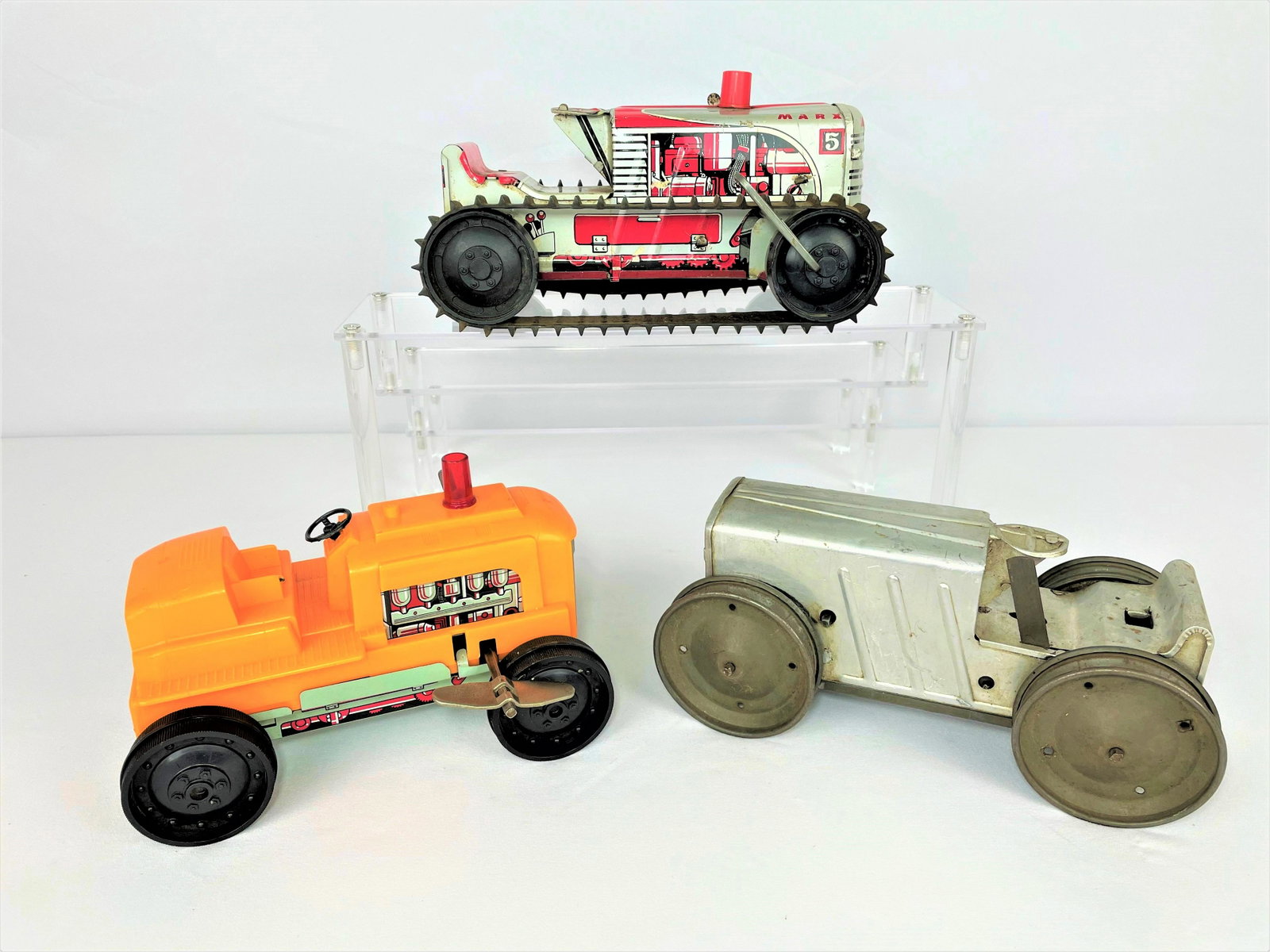 Antique & Vintage Marx Toy Tractors: Three (3) Marx toy tractors including a 1950s wind-up "Sparkling Climbing Tractor", an antique 1920s pressed steel wind-up tractor, and a 1950s orange plastic wind-up tractor. Missing figures. Antique