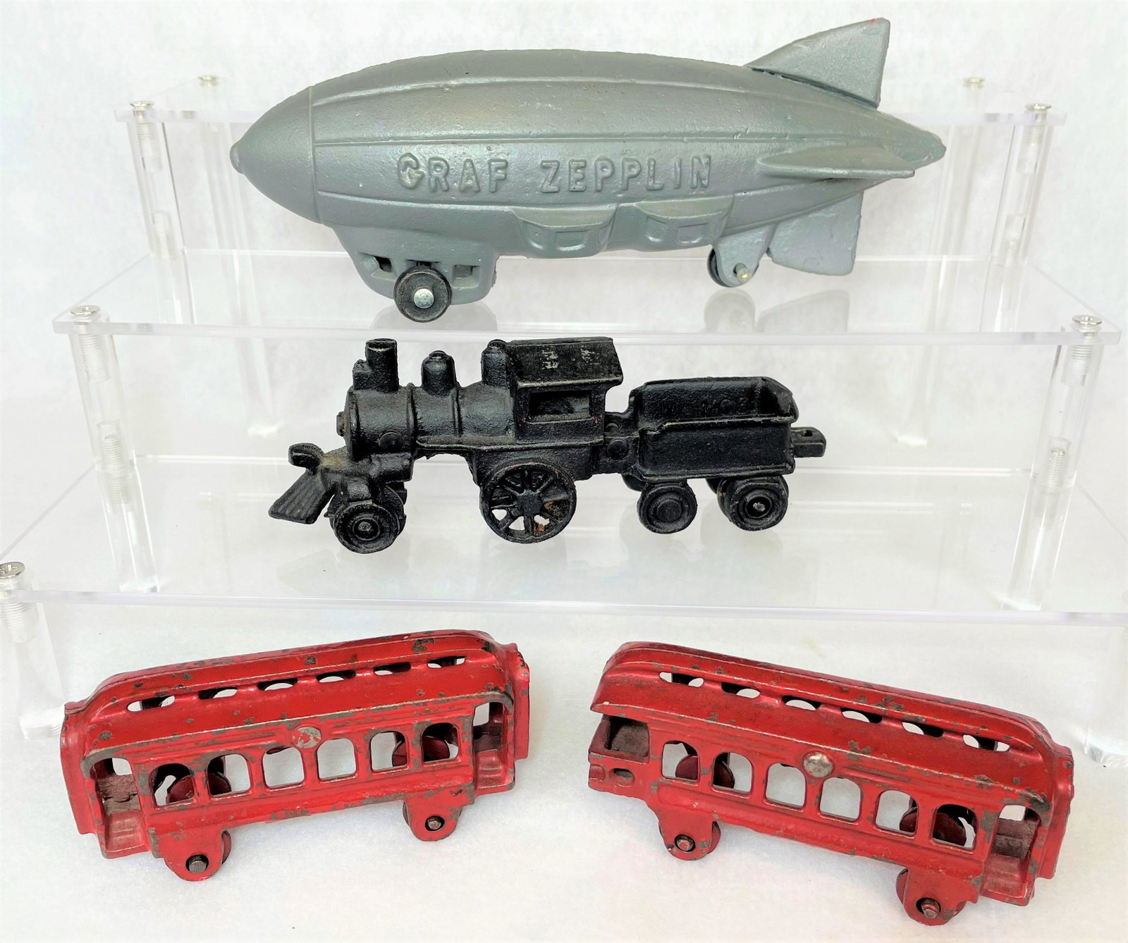 Group Vintage Cast Iron Toys Graf Zepplin: Group of four (4) vintage cast iron toys including a Graf Zepplin blimp, black locomotive, and two (2) red trolley cars. No makers marks noted. Very good condition. Some paint loss on trolleys as seen