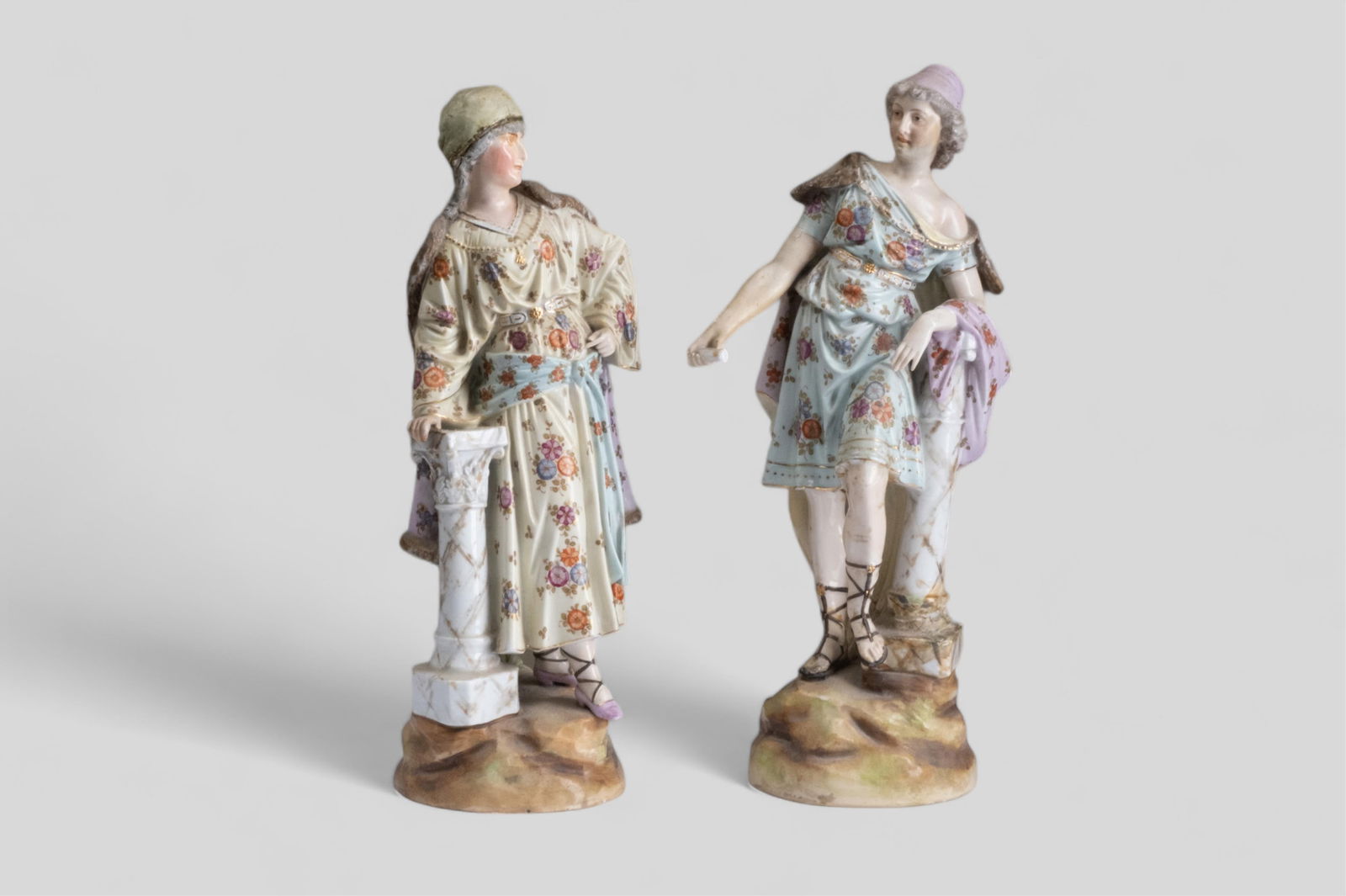Pair of Leaning Meissen Style Porcelain Figures: Pair of Leaning Meissenish Porcelain Figures of Male and Female The male figure is dressed in classical attire, including a soft, patterned tunic adorned with floral motifs and a cape draped over one