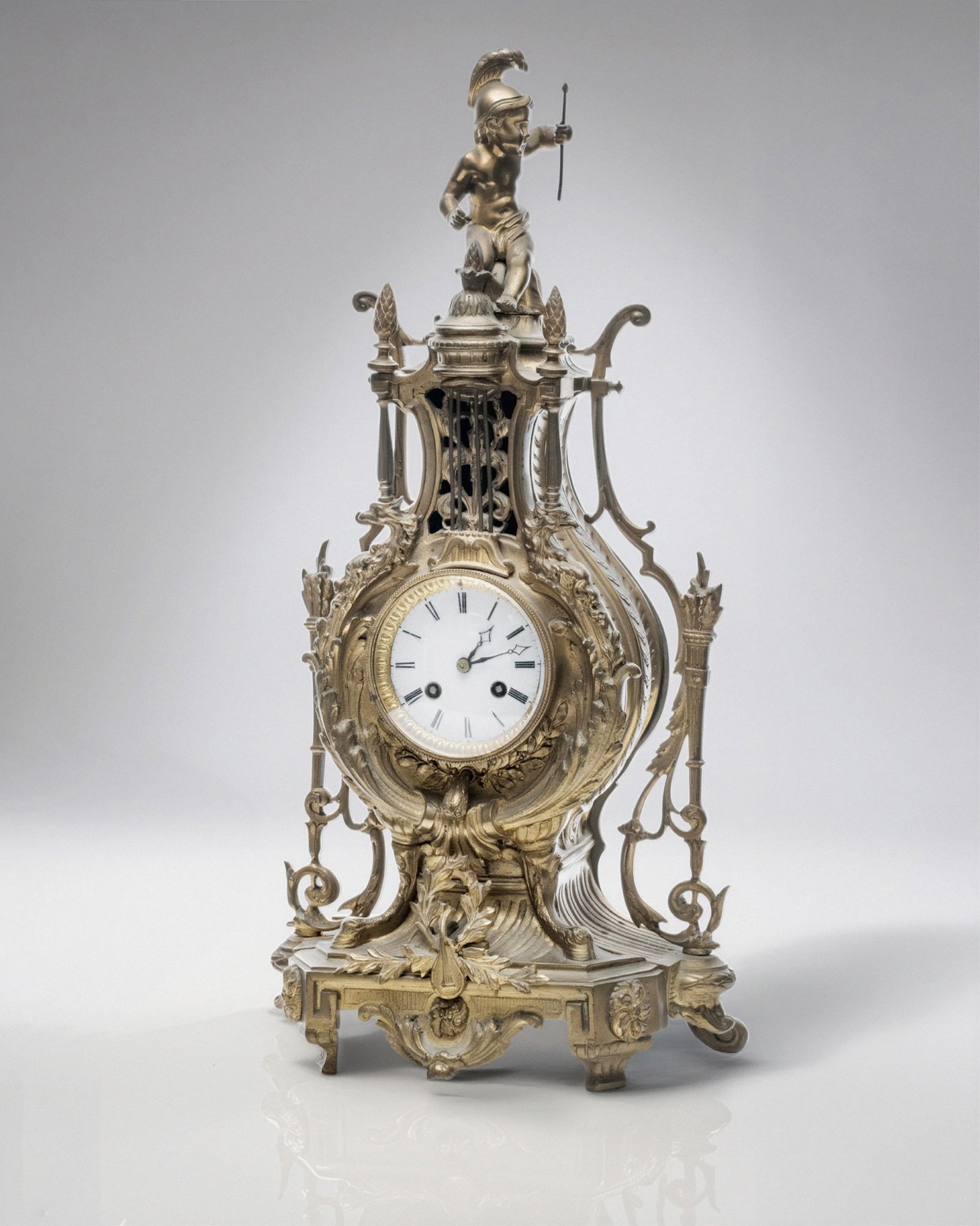 French Bronze Tall Mantel Clock Lyre Form Surmounted by Cupid Figure, 19th Century: Keywords: Mantel Clock, Lyre Form, Cupid Figure, Porcelain Face, Pendulum, Antique Timepiece, Decorative Clock, French Craftsmanship, has pendulum Summary: Fine 19th Century French Lyre form bronze