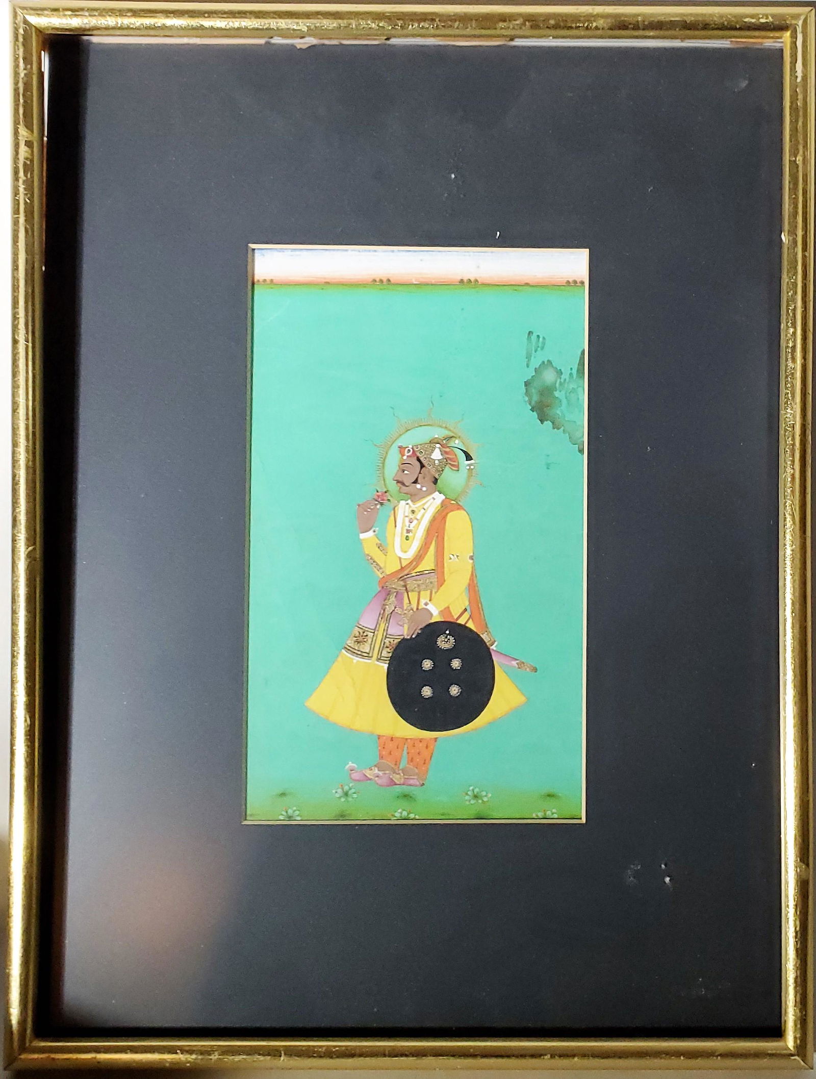 Indian Mughal Miniature Portrait: Indian Subcontinent Mughal antique miniature of the portrait of a Warrior-Prince posing with his shield by his side and holding a flower betraying his softer, more tender side; painted all over with r